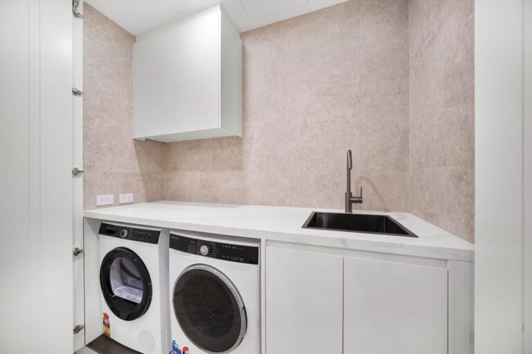 Laundry with stacked washer and dryer space, sink and white cabinetry in a LaCurva apartment
